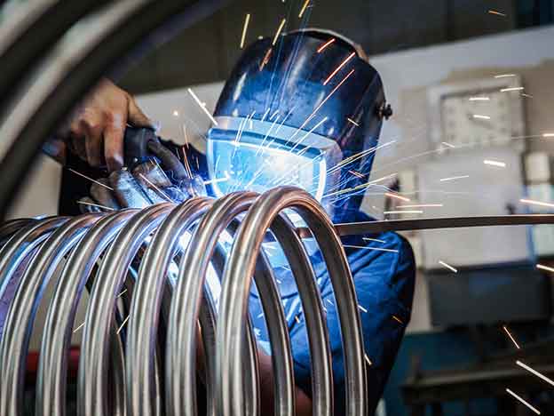 A welder wearing a protective helmet repairs an induction coil